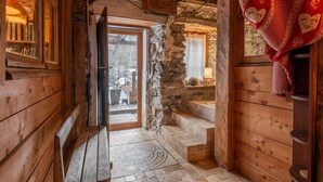 A rustic wooden interior with a stone wall, wooden bench, and a door leading outside.