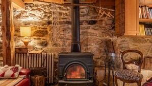 A stone-walled room with a wood-burning stove, a red leather sofa, a patterned chair, and a bookshelf.