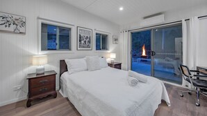 Une chambre dotée d’un grand lit, de deux tables de chevet avec des lampes, d’un fauteuil et d’une porte-fenêtre coulissante donnant sur un espace extérieur avec un foyer.