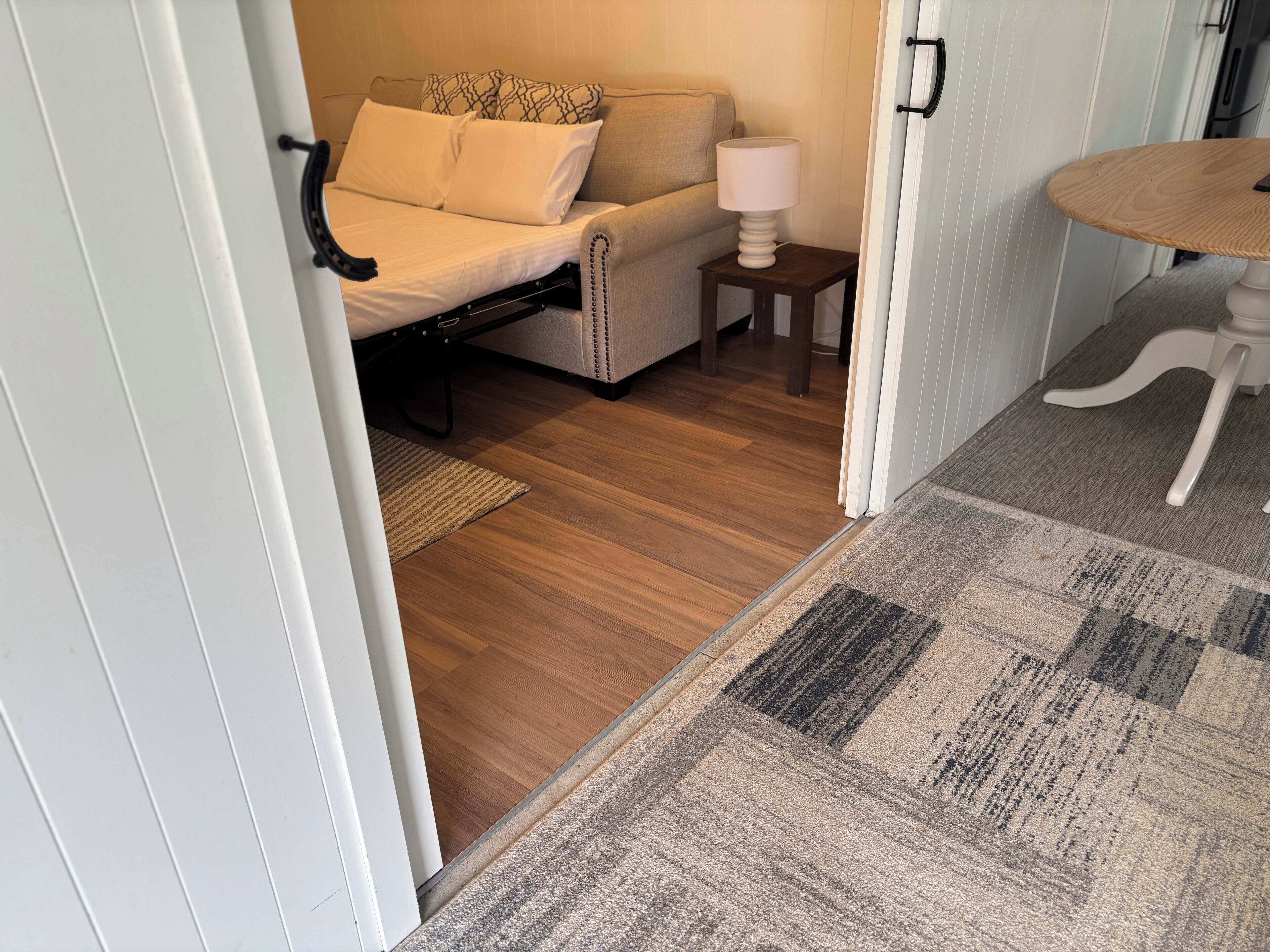 Un dormitorio con cama, mesita de noche, lámpara y una pequeña mesa con silla.