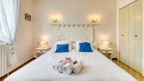 Ein ordentlich bezogenes Bett mit weißer und blauer Bettwäsche, zwei Nachttische und ein Satz zusammengerollter Handtücher auf dem Bett.