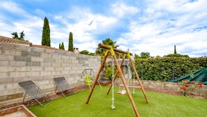 Ein Garten mit Schaukel, zwei Liegestühlen und einer Backsteinmauer.