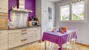 Eine Küche mit violettem Wandfarbton, einer Mikrowelle, einem Wasserkocher und einem Tisch mit Stühlen.