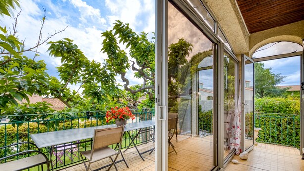 Eine überdachte Terrasse mit Tisch und Stühlen, einem Blumentopf und Blick auf die grüne Umgebung.