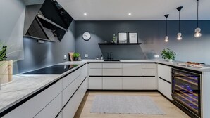 Une cuisine moderne avec des meubles blancs, un four encastré et des luminaires suspendus.