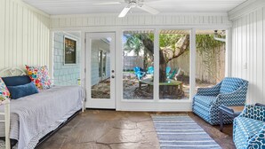 Un solarium con una cama, un ventilador de techo, una zona de patio con sillas y vista al jardín trasero.