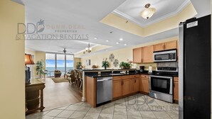 A spacious kitchen with wooden cabinets, a stainless steel refrigerator, and a large island. - Sienna on the Coast 1006 | Enjoy Beautiful 10th Floor Views of the Gulf! (Gulfport)