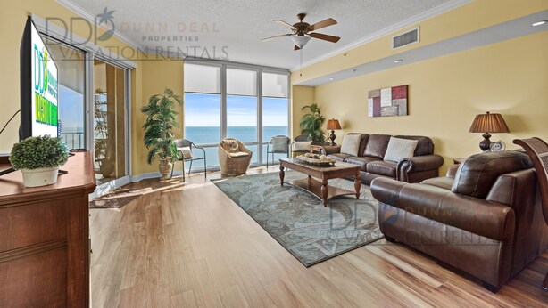 A spacious living room with a large window, a ceiling fan, and a view of the ocean. - Sienna on the Coast 1006 | Enjoy Beautiful 10th Floor Views of the Gulf! (Gulfport)