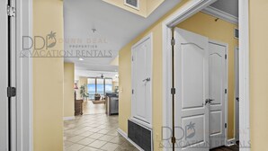 A hallway with a tiled floor leading to a kitchen area. - Sienna on the Coast 1006 | Enjoy Beautiful 10th Floor Views of the Gulf! (Gulfport)