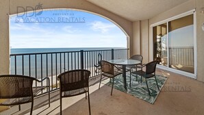 A balcony with a view of the ocean, furnished with wicker chairs and a table, and a sign for vacation rentals. - Sienna on the Coast 1006 | Enjoy Beautiful 10th Floor Views of the Gulf! (Gulfport)