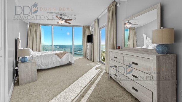 A spacious bedroom with a large bed, a vanity with a mirror, and a view of the ocean. - Sea Breeze 907 | Condo Directly on the Beach! (Biloxi)