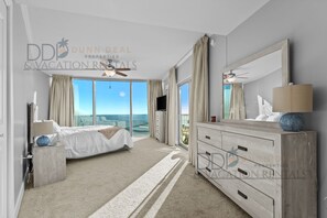 Een ruime slaapkamer met een groot bed, een kaptafel met spiegel en uitzicht op de oceaan.