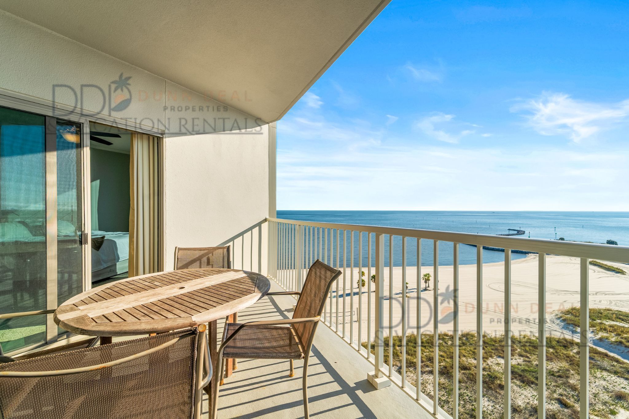 Un balcon avec une table et des chaises, donnant sur une plage et l’océan.