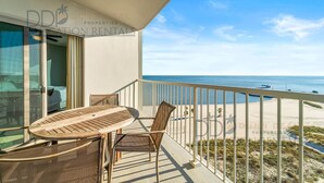 A balcony with a table and chairs, overlooking a beach and ocean. - Sea Breeze 907 | Condo Directly on the Beach! (Biloxi)