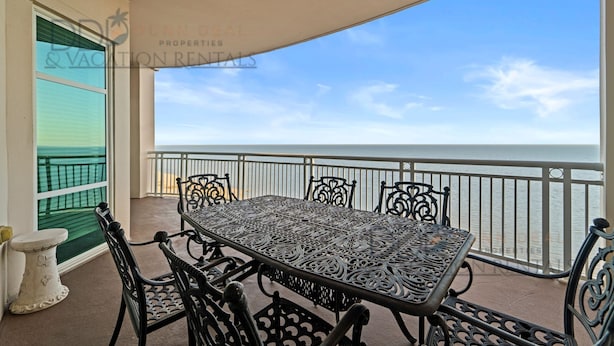 A balcony with a table and chairs, overlooking a body of water. - Legacy Tower I 1403 | Penthouse Unit Overlooking the Beautiful Gulf! (Gulfport)