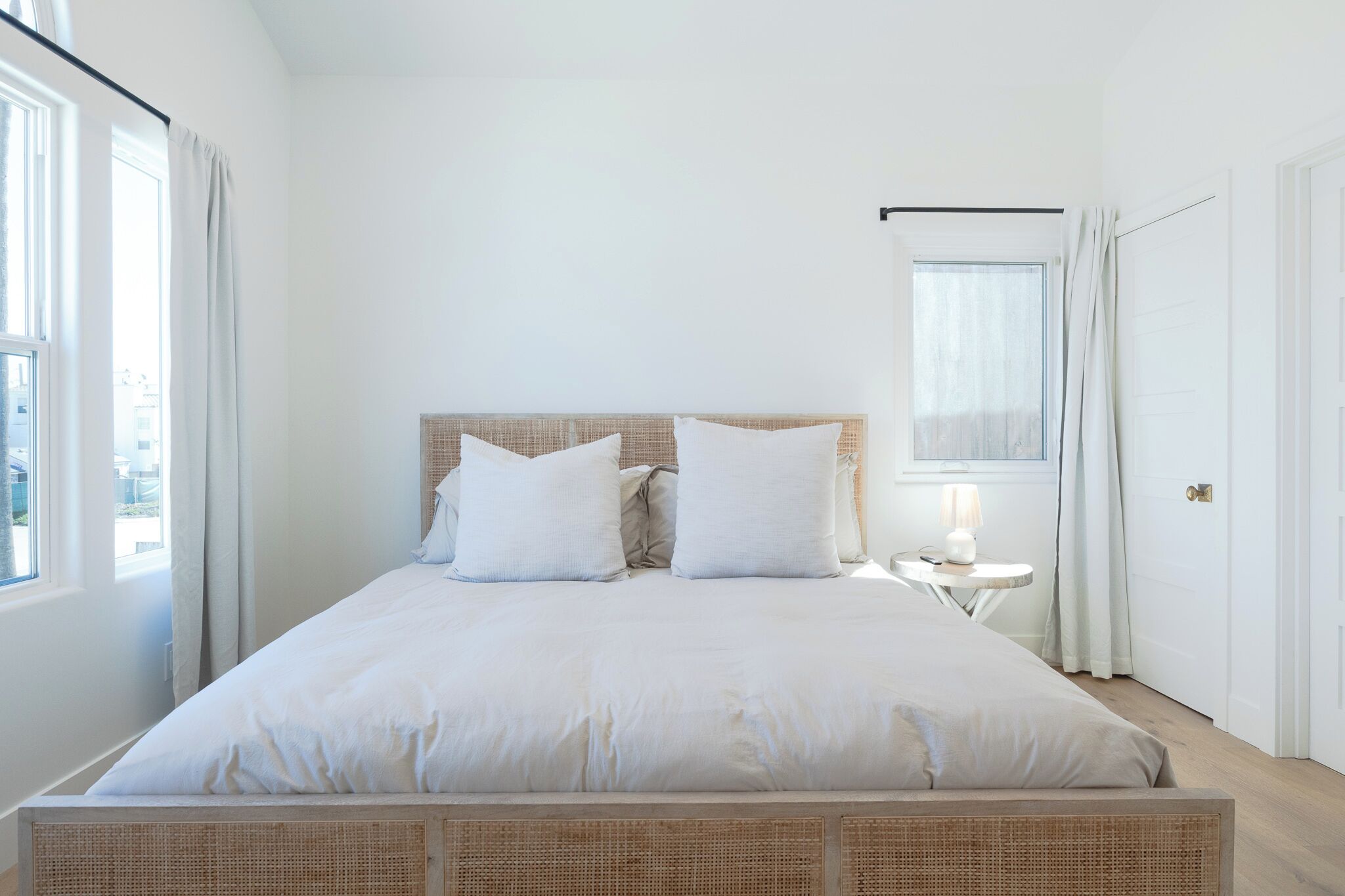Ein ordentlich eingerichtetes Schlafzimmer mit einem großen Bett, einem Nachttisch mit Lampe und einem Fenster mit Vorhängen.