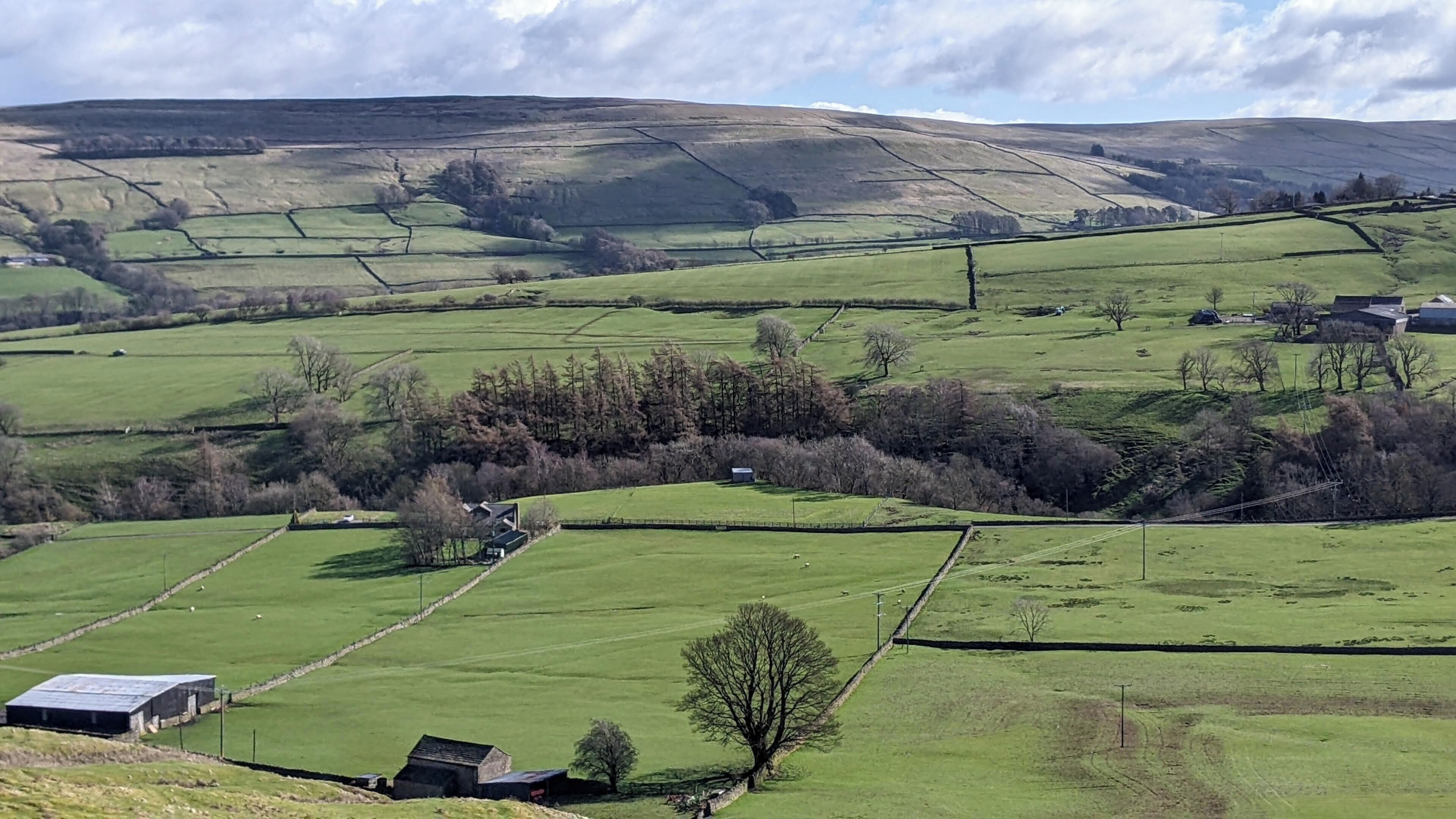 A rural landscape with rolling hills, fields, and scattered buildings.