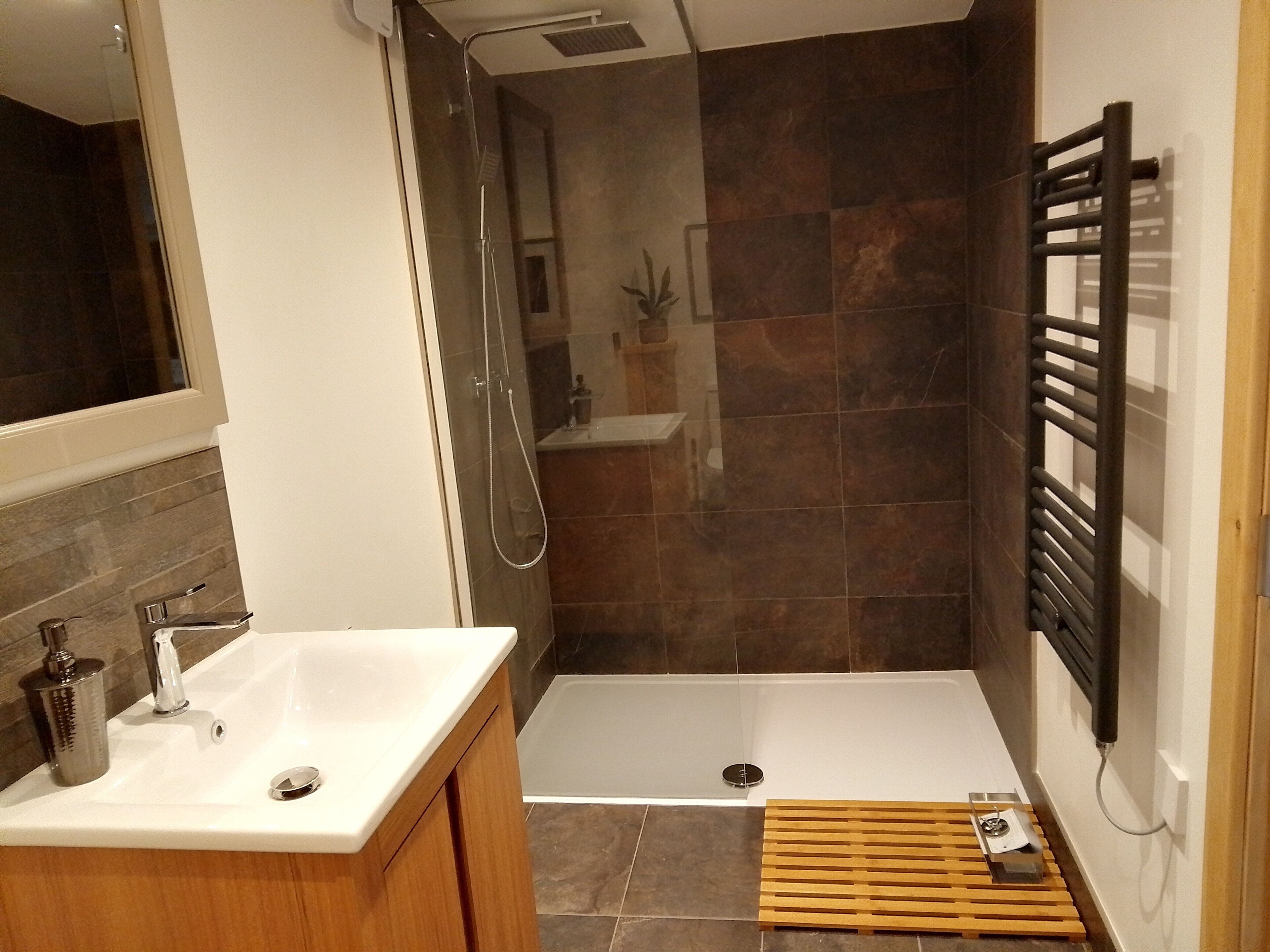 Un baño moderno con ducha, lavamanos y un banco de madera.