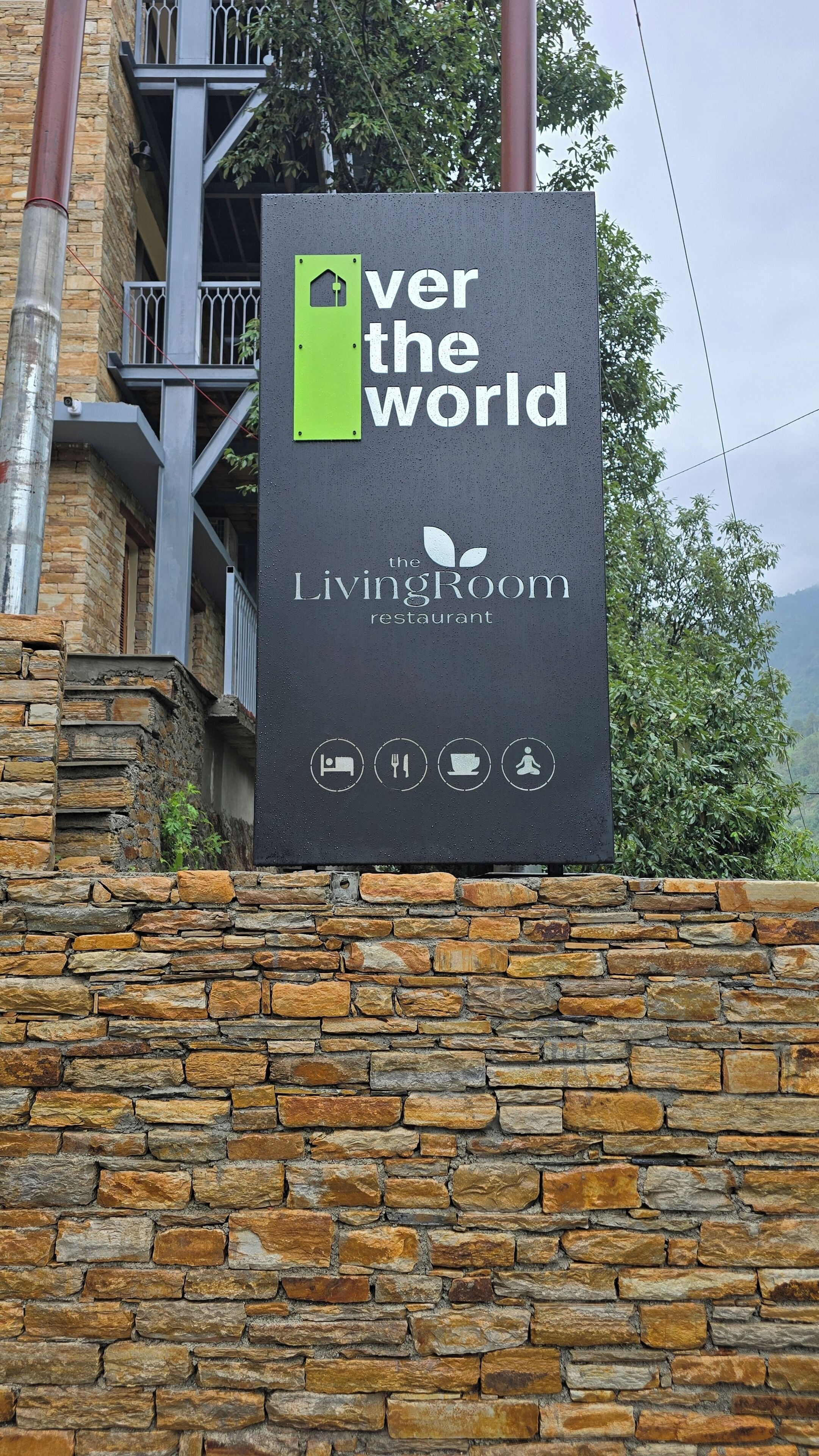 A sign for 'LivingRoom Restaurant' with a stone wall and metal railing in the background.