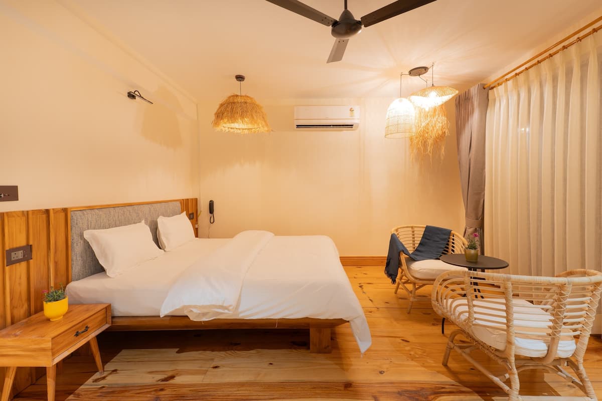 A bedroom with a bed, wooden nightstand, wicker chairs, a small table, and a ceiling fan.