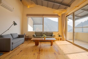 A room with a sofa, a coffee table, a lamp, and a view of mountains through large windows. - Over The World (Kosiyakutoli)