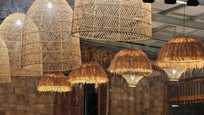 A restaurant interior with stone walls, wicker chairs, and hanging wicker lamps. - Over The World (Kosiyakutoli)