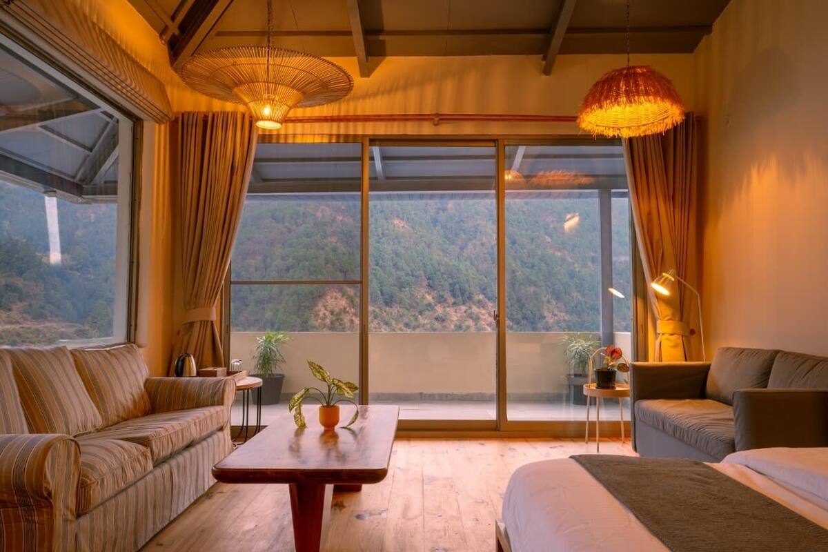 A room with a large sliding glass door, a sofa, a bed, a small table, and a hanging light fixture.