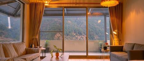 A room with a large sliding glass door, a sofa, a bed, a small table, and a hanging light fixture.