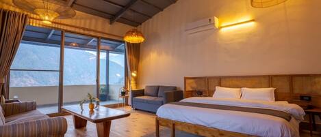 Habitación de hotel con una cama grande, un sofá, una mesa y vistas a las montañas.