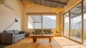 A living room with a sofa, a coffee table, a floor lamp, and a view of mountains through large windows. - Over The World (Kosiyakutoli)