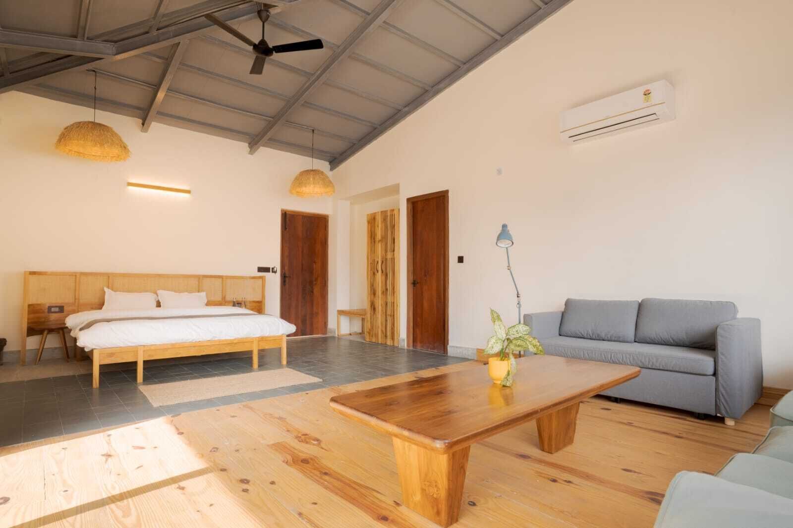 A room with a bed, a sofa, a wooden coffee table, a hanging light, and an air conditioning unit.