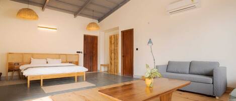 A room with a bed, a sofa, a wooden coffee table, a hanging light, and an air conditioning unit.
