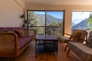 A room with a sofa, a table, and two chairs, a large window with a mountain view, and a balcony with a metal railing. - Over The World (Kosiyakutoli)