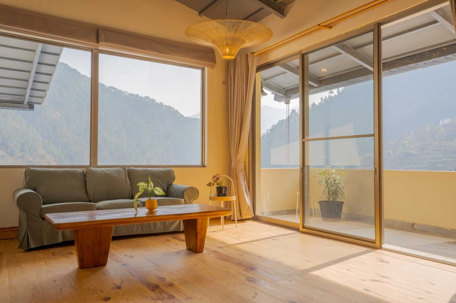 Une pièce comprenant un canapé, une table basse en bois, une plante en pot et de grandes fenêtres donnant sur une vue sur les montagnes.