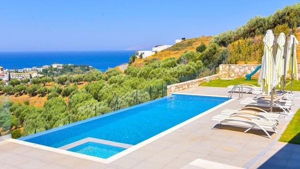 Une piscine avec vue sur la mer, entourée d’une terrasse agrémentée de chaises longues et de parasols.