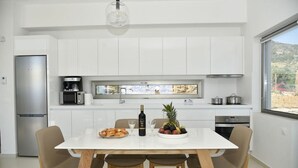 Une cuisine moderne avec des meubles blancs, un réfrigérateur en acier inoxydable, une machine à café et une table à manger avec des chaises.