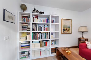 Una habitación con una estantería blanca llena de libros, un sofá rojo, una mesita de madera y una lámpara.