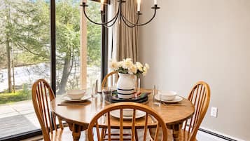 Uma sala de jantar com uma mesa redonda de madeira, quatro cadeiras, um lustre e um vaso com flores.