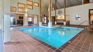 Ein Hallenbad mit gefliestem Boden, Holzbalkendecke und einer großen Wanduhr.