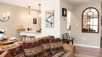 A living room with a sofa, dining table, chandelier, and a poster on the wall.