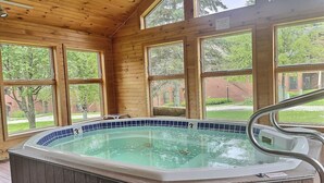 Eine Holzterrasse mit Whirlpool, großen Fenstern und Blick auf ein Backsteinhaus.