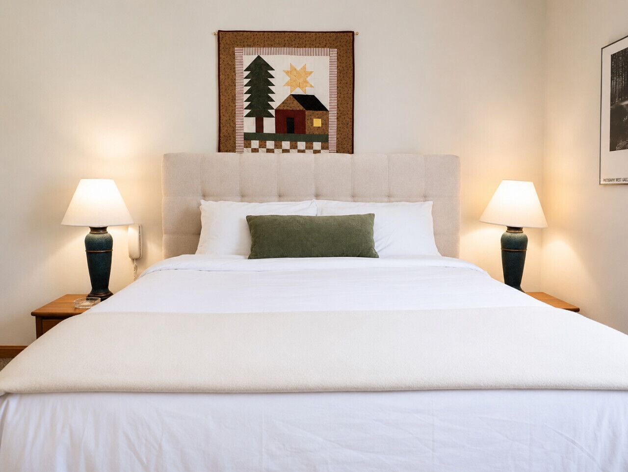 A bed with a white duvet, two bedside lamps, and a framed picture above it.