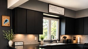Cozinha moderna com armários escuros, uma ilha grande com banquetas, uma janela com luz natural e uma placa com a inscrição 'Seja nosso convidado'.