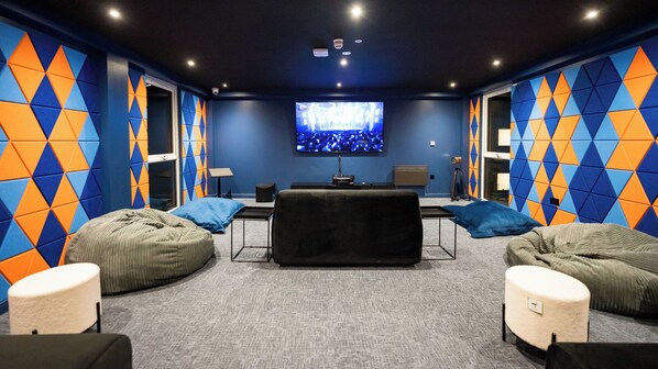 Una habitación moderna con una televisión de pantalla plana grande, sillones tipo bean bag y una pequeña mesa.
