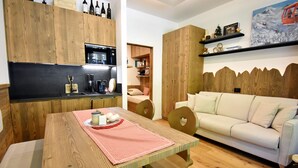 Un espace de vie compact comprenant une table à manger en bois, un canapé et un coin cuisine avec des meubles en bois et un four à micro-ondes.