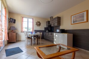 A compact kitchen with a dining table, chairs, a TV, and a refrigerator. - Gîte la Combe Verte – Renovated Farmhouse with Indoor Pool (Claveyson)
