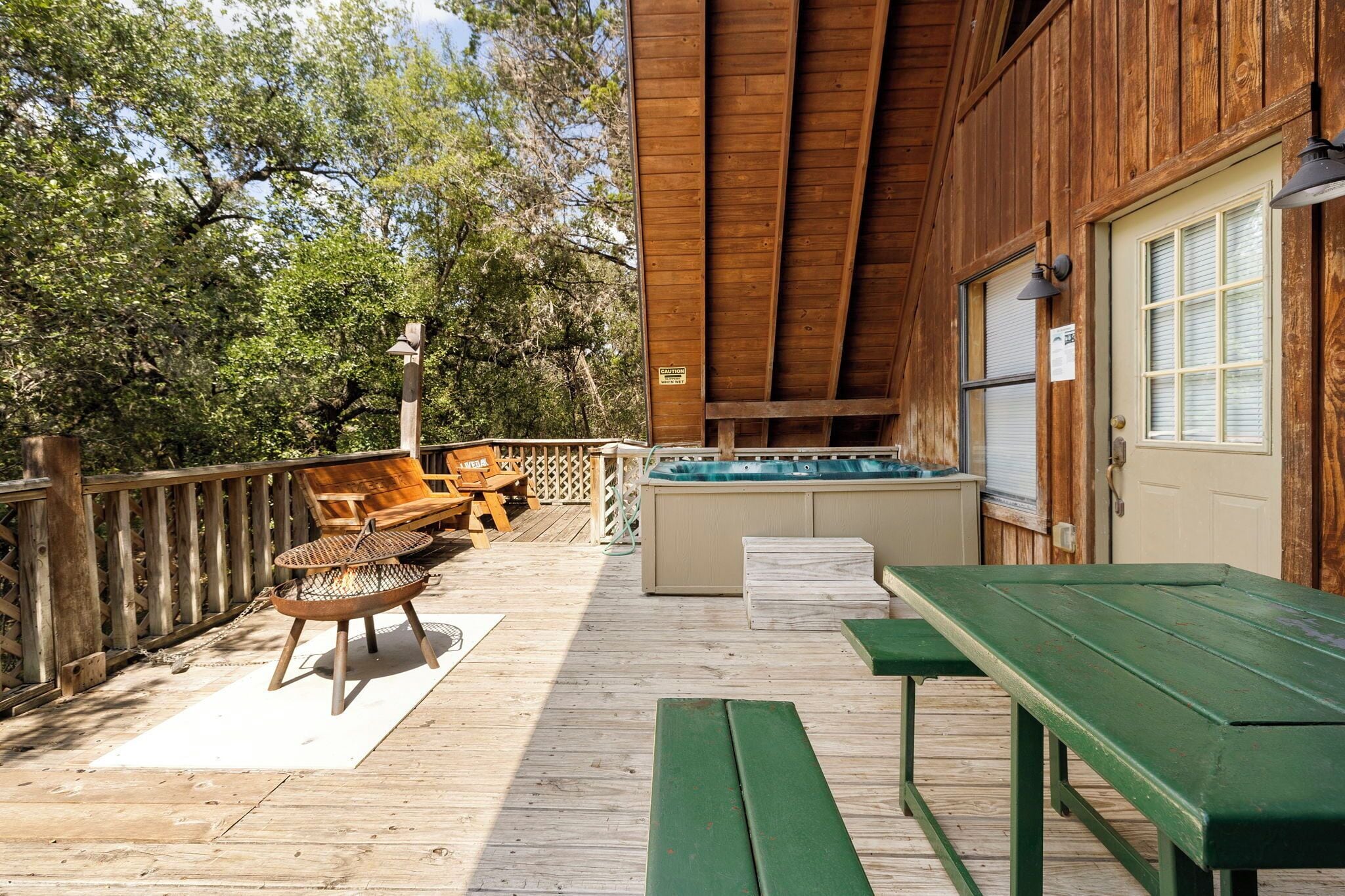 A wooden deck with a hot tub, wooden chairs, and a table.