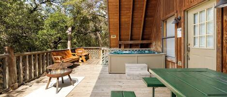 A wooden deck with a hot tub, wooden chairs, and a table.