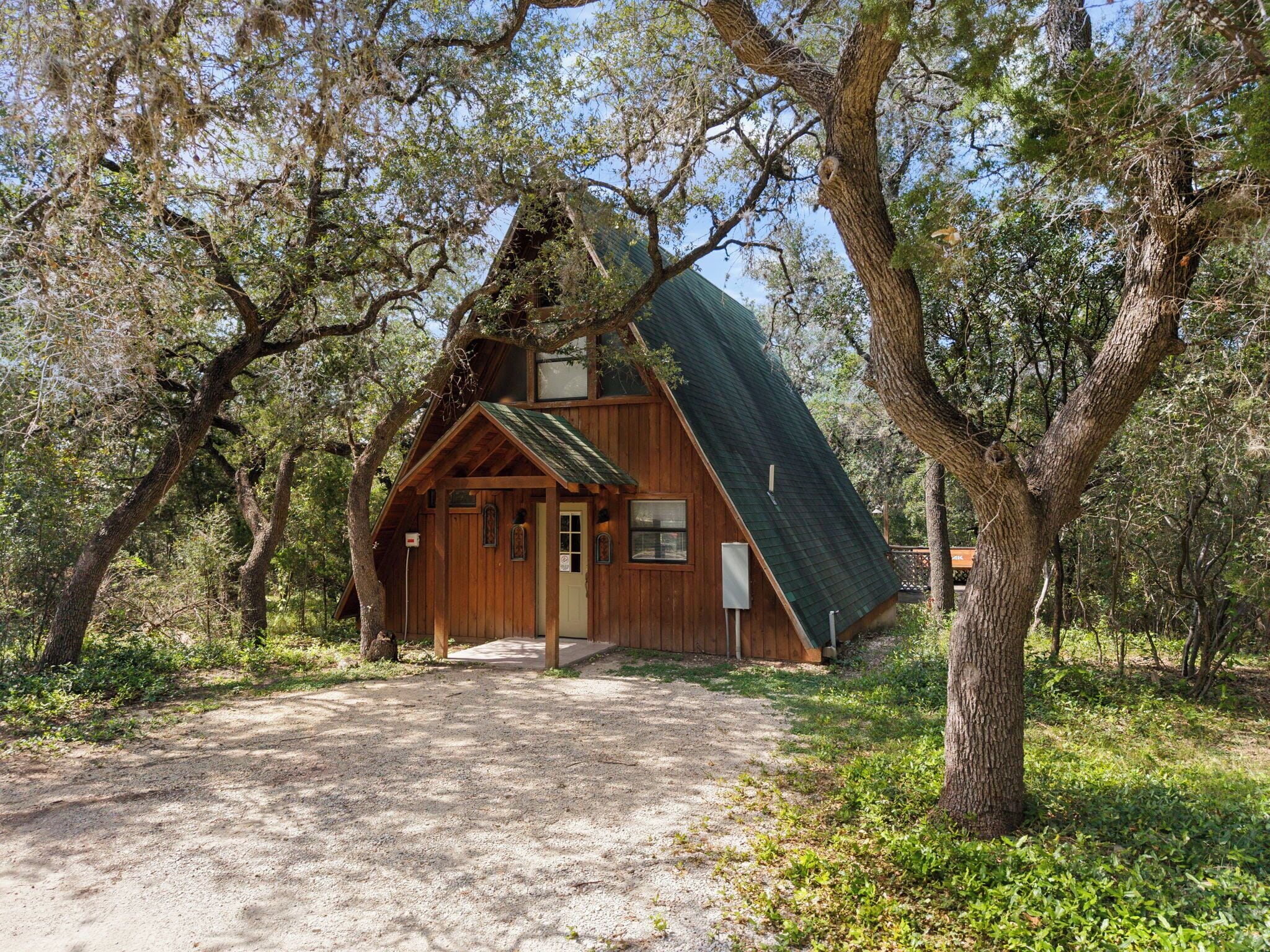 A rustic cabin with a steeply pitched roof, surrounded by trees.
