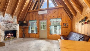 Ein Interieur einer Hütte mit Kamin aus Stein, Holzwänden und Holzboden, einem Fernseher und einem Sofa.